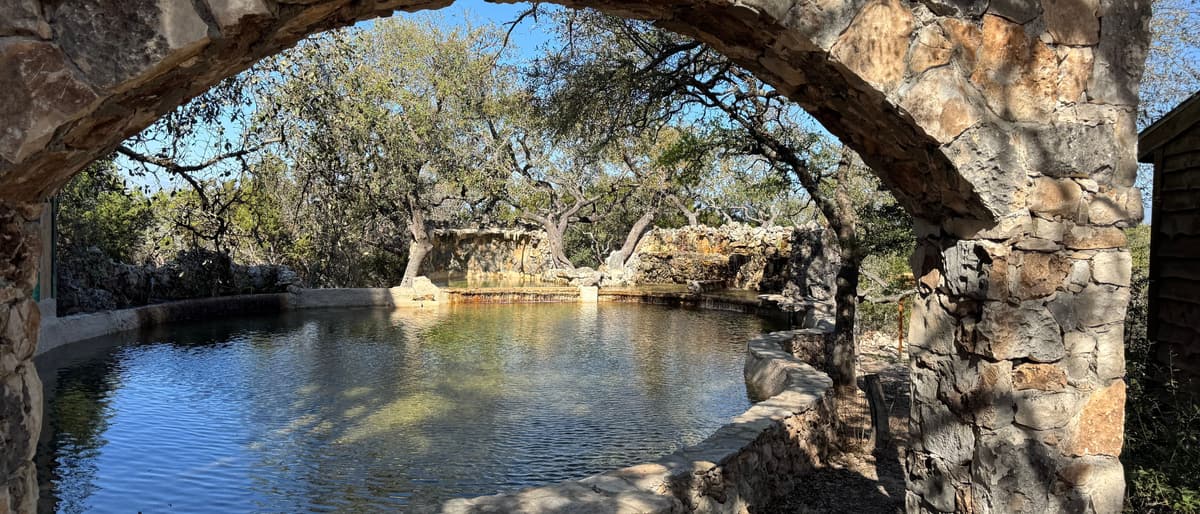 A hand-built stone arch opening onto still water and old live oaks.