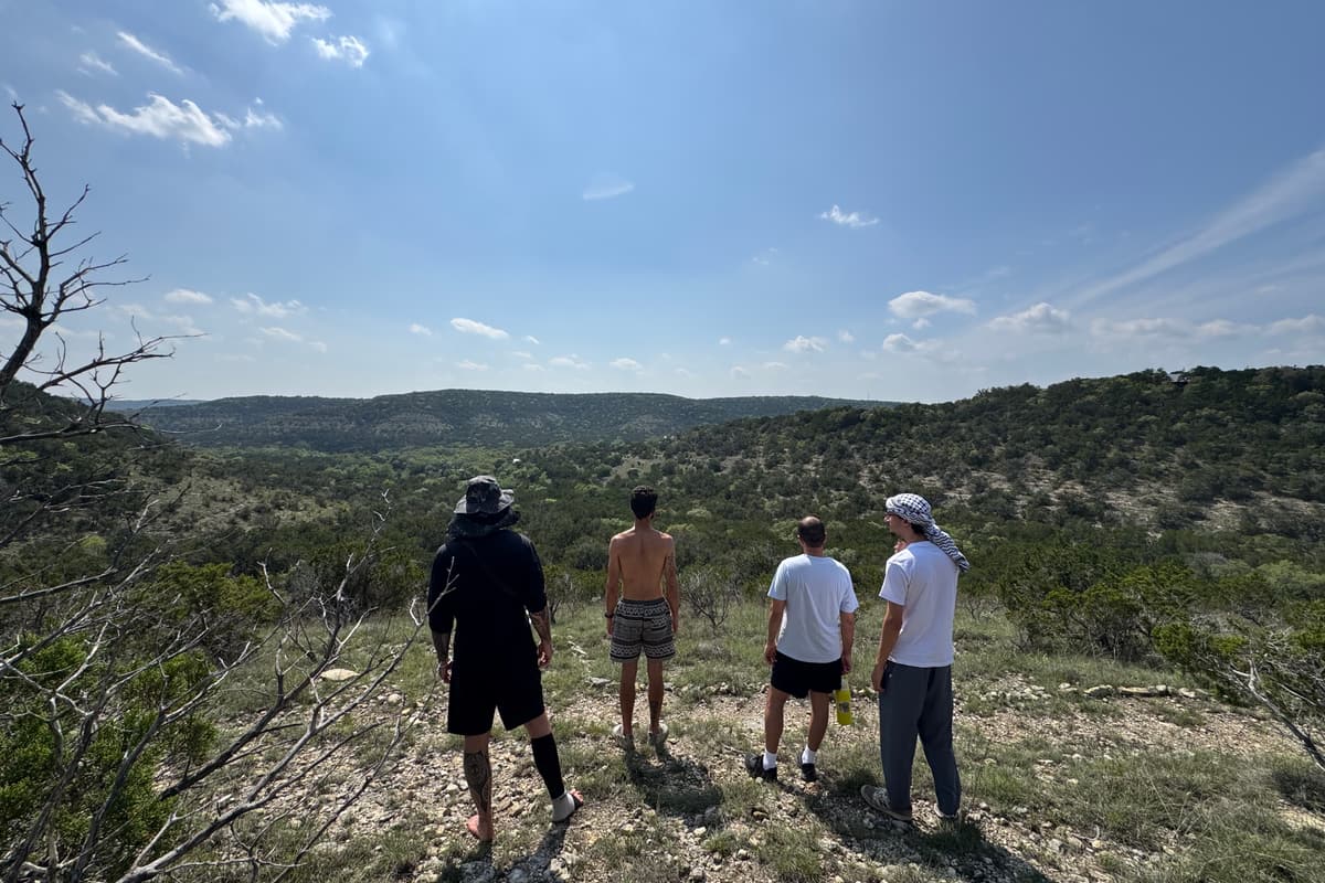 Four men seen from behind, standing together on a rocky ridge and looking out over the hills.