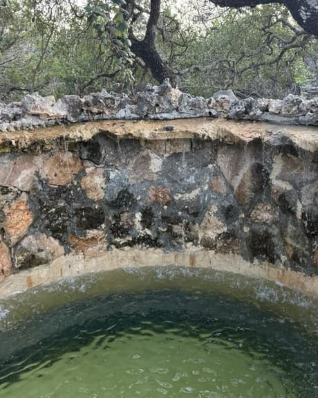 The round stone hot tub, its water clear green against a curved rock wall.