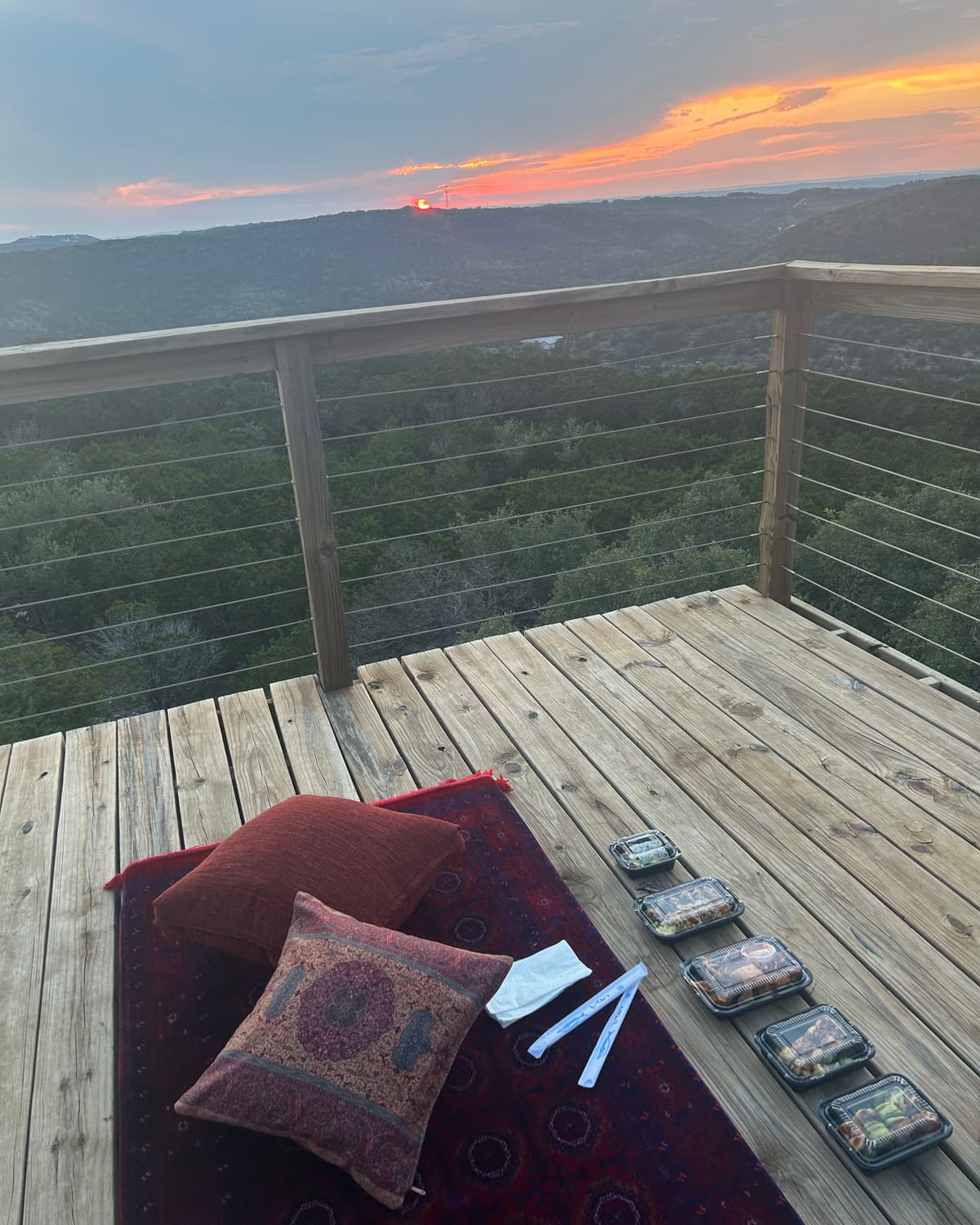 Floor cushions and candles laid out on the rooftop deck at sunset, the hills fading into the distance.