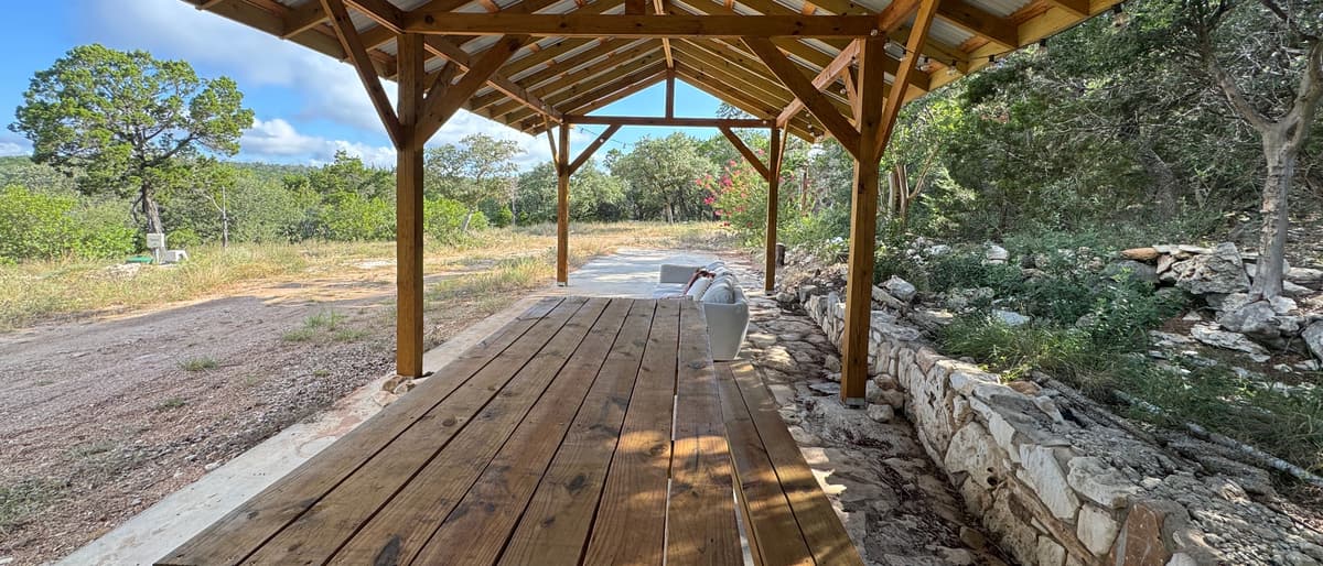 A long wooden table under an open-air pavilion, looking out over the trees.